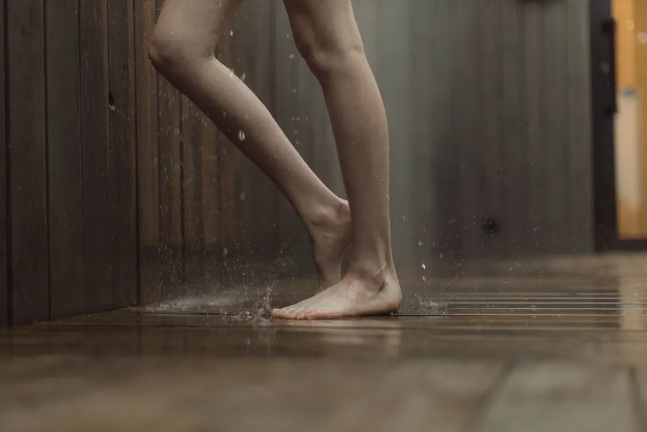 Close-up of a person standing barefoot on a wet wooden floor indoors.